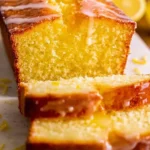 Slice of the best lemon loaf with a glaze on a wooden cutting board